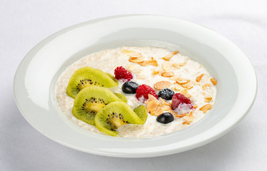 Oatmeal breakfast with berries and kiwi on white background