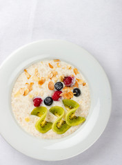 Oatmeal breakfast with berries and kiwi on white background