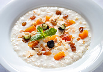 Oatmeal breakfast with raisins, dried apricots and peanuts on white background