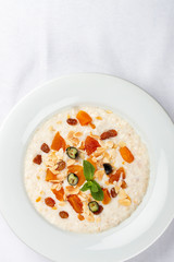 Oatmeal breakfast with raisins, dried apricots and peanuts on white background