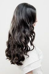 Naklejka premium Black long hair of a girl from a back against a white wall