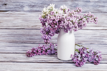 Blooming Lilac flowers in white vase on wooden background with copy. Bouquet of flowers as spring gift. Selective focus.