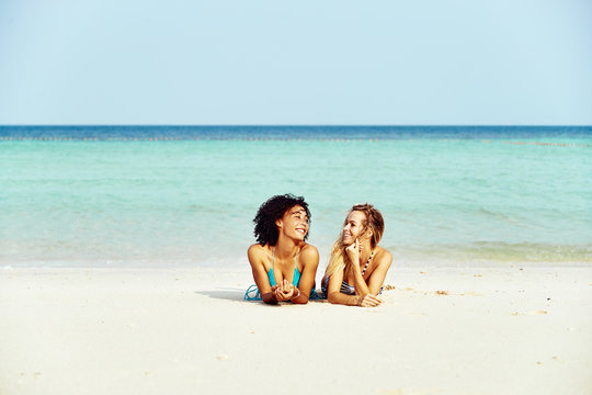 Smiling friends in bikinis suntanning on a tropical beach