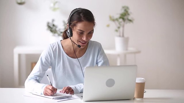 Happy woman in headphones speaking by webcam making notes