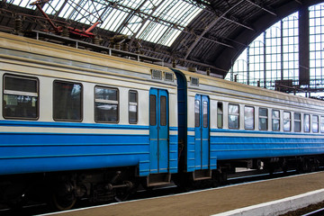 Fototapeta na wymiar Blue cars of an electric train stopping under the roof of a covered apron of the railway station.