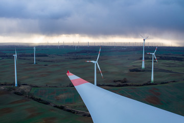 Remote wind farm seen from eye level with rotor blade in the foreground with dark clouds and rain...