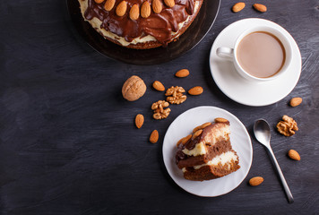 Homemade chocolate cake with milk cream, caramel and almonds on black wooden background. cup of coffee.