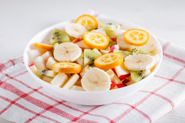 Vegetarian salad of bananas, apples, pears, kumquats and kiwi on linen tablecloth, close up, selective focus.