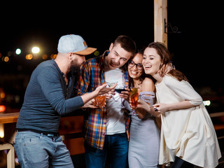 friends with smiles on their faces in the bar have fun, drink cocktails, clink glasses.