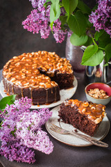 Table with homemade Chocolate cake with caramel and peanuts and Lilac flowers