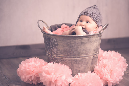 Portrait s&uuml;&szlig;es Baby sitzt im Eimer mit M&uuml;tze rosa Ponpons