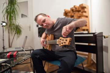 Musician tuning electric guitar in home music studio.