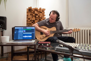 Musician playing electric guitar in home music studio.