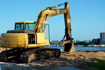 Fototapeta na wymiar A yellow front end bucket loader excavator sits on land at the water's edge at bay in Bonita Springs Florida on a sunny morning.