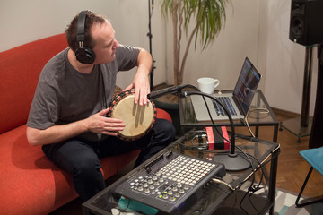 Musician playing djembe drum instrument in home music studio.