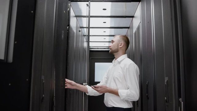 Caucasian man open server rack and checking data center slow motion. Serious system administrator looking to mining farm and diagnostic cloud infrastructure standing before the modern datacenter