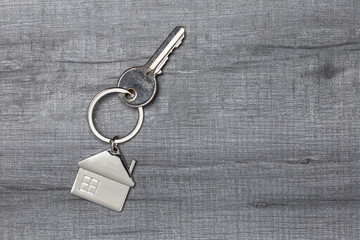 House keychain and key on wooden table with copy space