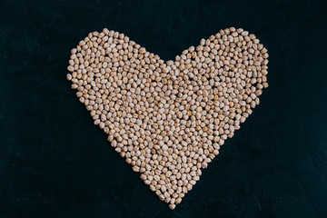 Raw chickpea in form of heart isolated on black bacground. Organic grown. Raw protein. Vegan healthy ingredient. Nutritious food. Uncooked garbanzo