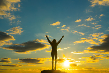 Silhouette of a girl with raised arms goes to the horizon, against the backdrop of a dramatic sky in the sunset. Concept of success and achievement. winner, good luck. Travel outdoors. business