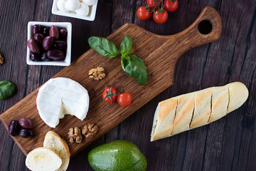 Fototapeta na wymiar Camembert cheese, bread, olives, walnut, mozzarella,basil and cherry tomatoes on brown wooden board. Mediterranean kitchen.