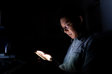 Asian man addict using smartphone all time.  Using a devices in dark is not good for eyes and healthy.