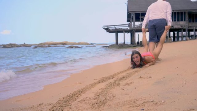 male pulls a girl along the seashore, the girl resists and wants to rest further, the concept of the end of the holiday, the concept of starting to work.