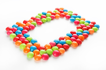Frame of multi-colored candies close up. Rainbow colored dragee multicolored glaze on a white background