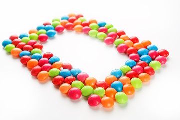 Frame of multi-colored candies close up. Rainbow colored dragee multicolored glaze on a white background