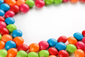Frame of multi-colored candies close up. Rainbow colored dragee multicolored glaze on a white background