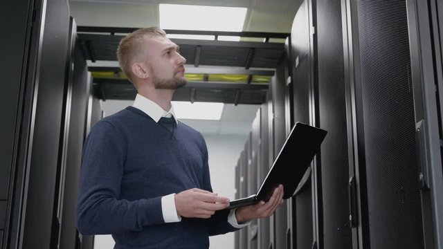 Man holding laptop and do diagnostic of datacenter in server room. Engineer standing in corridor and working with cyberspace system and hardware database. Networking administrator service a big data