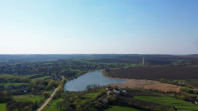 Aerial flying over beautiful rural Europe landscape early spring with fields, buildings, ponds and trees. Sunset time, panoramic video 4k.