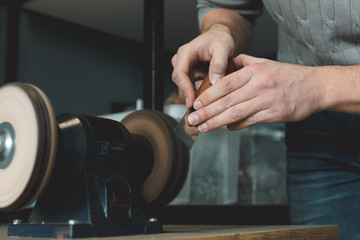 Close up of leather craftsman sharpens knife for cutting leather on sander. Handmade concept. Concept of small business to create leather products.