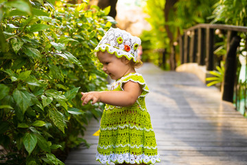 little girl in a knitted dress, chamomile, looks at the green leaves, the concept of children fashion