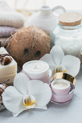 Organic cosmetics with coconut oil, sea salt, towels and handmade soap with white orchid flowers on grey background