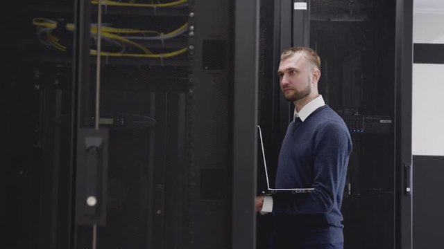 Server system support administrator walking in room of data center and control the database using internet and laptop. Professional IT engineer working in mining farm infrastructure hardware storage