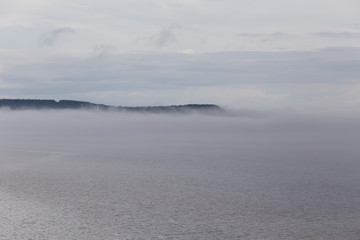 Beautiful atmospheric early morning landscape with mist rising over the St. Lawrence Gulf waters in a northern Anticosti Island bay, with a cape in the background