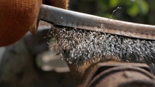 Close-up of a man's hands in work gloves, cleaning the old pipe from rust with a metal brush.