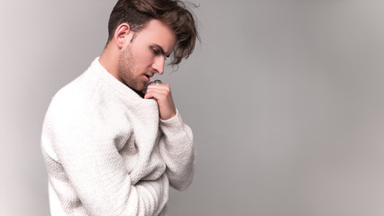  Beautiful portrait of a young guy who thought about something. Men's model tests on a white background. Wearing a white sweater.