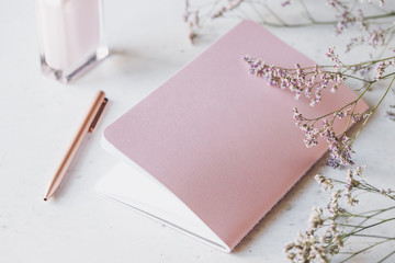 Pink empty paper notebook with golden pen on white table surrounded by flowers and fragrance. The concept of femininity workplace