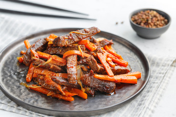 Close-up of Chinese spicy Szechuan beef meal on a black plate with wooden sticks over white table....