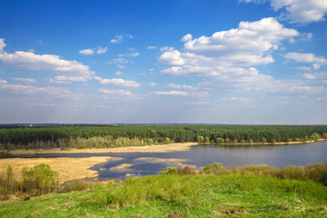 Beautiful view of river, green forest and blue cloudy sky from the top of the hill. Spring landscape.