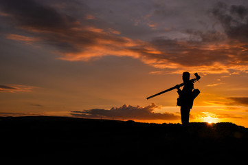 Silhouette of photographer with tripod against setting sun