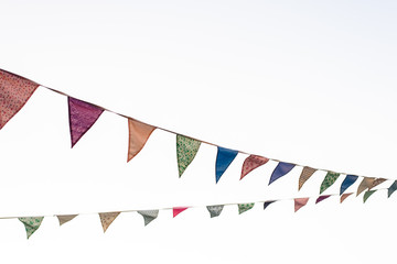 Pennants with blue sky background and pale colors hanging on a rope crossing the image during an...