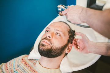 Barbershop theme. Hairdresser for washing hair in a barbershop. Hands male hairdresser close-up washes hair with foam and shampoo Caucasian man with beard