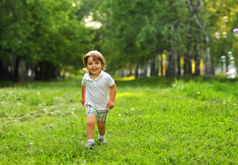 Beautiful 2 year old boy playing in the summer outside in the greenery with soap bubbles