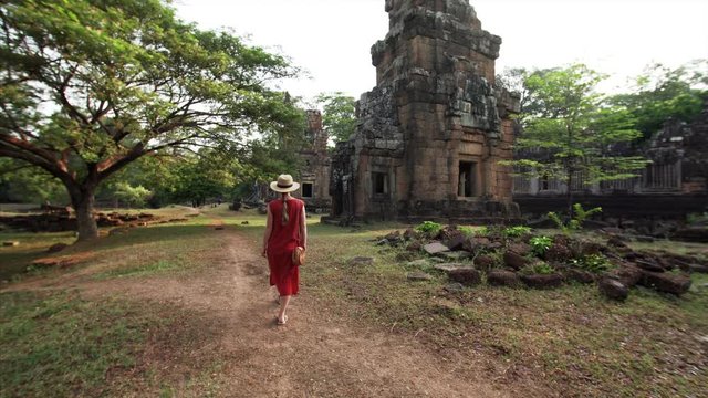 Following the woman in red dress who is exploring ruins of Prasat Suor Prat towers, a series of twelve towers in Angkor Wat complex, made from rugged laterite and sandstone. Cambodia