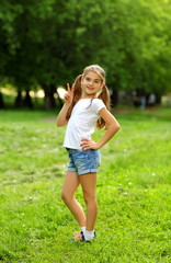 Naklejka na ściany i meble A charming girl in shorts and a t-shirt smiles in the summer against the green in the park