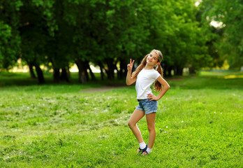 A charming girl in shorts and a t-shirt smiles in the summer against the green in the park