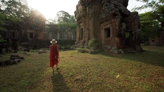Following woman who is exploring Prasat Suor Prat towers under beautiful sunshine. It's a series of twelve towers in Angkor Wat complex, made from rugged laterite and sandstone. Cambodia