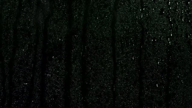 Many small drops on black glass curface coming down on black background, window condensation. Stock footage. Close up for water being sprayed on black window.